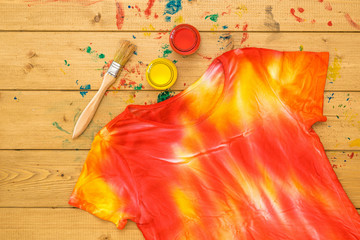 T-shirt decorated in tie dye style in yellow and red colors on a wooden table. Flat lay.