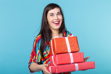 Slim beautiful young brunette girl holding a red gift boxes in her hands while standing against a blue background. Concept of shares and bonuses.