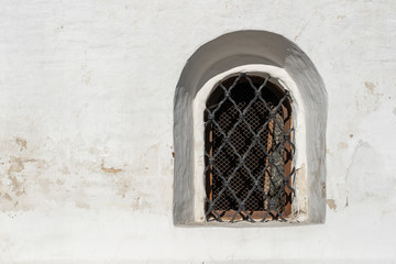 An ancient window in the white wall. Lattice on the window in the old style. Old-style architecture concept