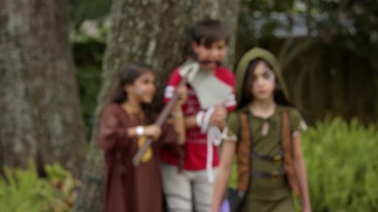 Two warrior girls have a boy tied up with an ax to his neck. One walks toward the camera and shoots a toy crossbow at the camera. Shot in 4k slow motion.
