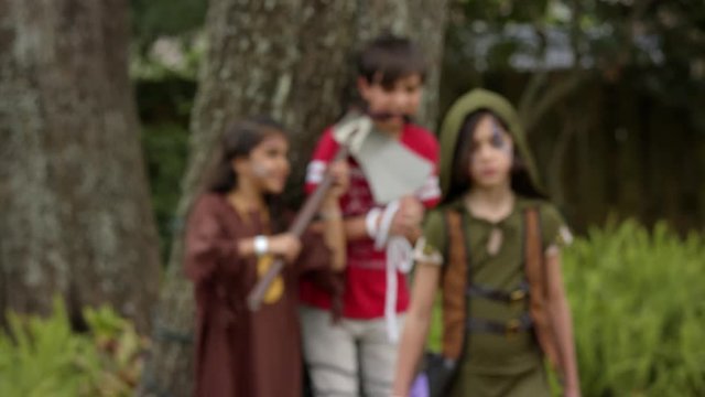 Two warrior girls have a boy tied up with an ax to his neck. One walks toward the camera and shoots a toy crossbow at the camera. Shot in 4k slow motion.