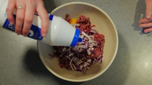 Female hands can be seen adding herbs to a burger mix. The mixture is then seen being mixed together.