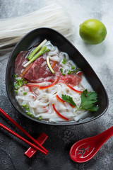 Bowl of traditional vietnamese pho bo soup, vertical shot over grey stone background