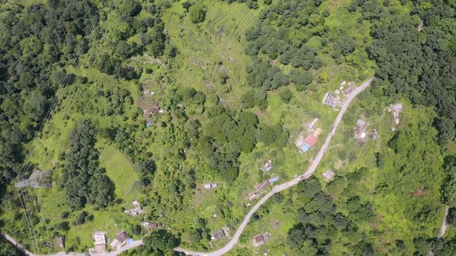 Aerial, top down, drone shot, over buildings, in a small town, on a mountain, surrounded by Indian forest, on a partly sunny day, in Sikkim, India