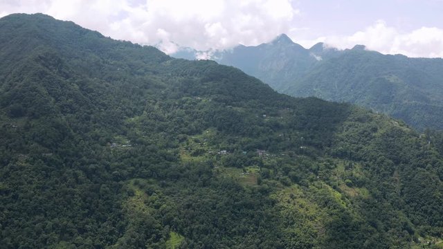 Aerial, drone shot, towards a group of houses, in a small village, on a mountain wall, surrounded by Indian forest, on a partly sunny day, in Sikkim, India