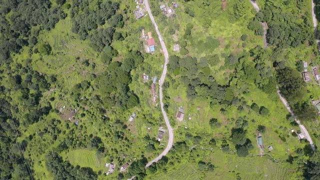 Aerial, top down, drone shot, over buildings and vehicles, in a small town, on a mountain, surrounded by Indian forest, on a partly sunny day, in Sikkim, India