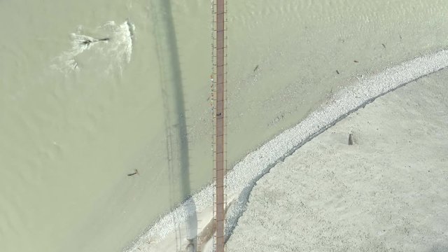 Aerial, birdseye, drone shot, rising above a Lepcha clan man walking on a suspension bridge, over Tista river, on a sunny day, in Sikkim, India