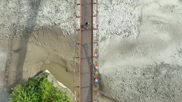 Aerial, top down, drone shot, rising above a Lepcha clan man walking on a suspension bridge, over Tista river, on a sunny day, in Sikkim, India