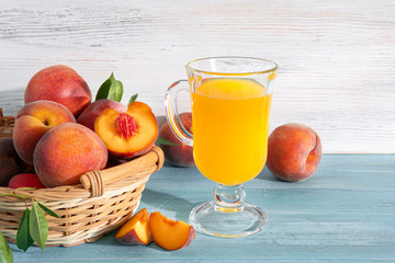 Glass of juice and Sweet ripe juicy fruit, peaches with green leaves in basket on blue background