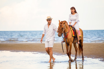 Young couple in love walking with the horse at sea beach on blue sky . honeymoon tropical sea...