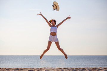 Obraz premium beautiful young asian woman excited throwing hats up on the air at the sea beach . Happy girl enjoy holidays vacation . success . winner .outdoors