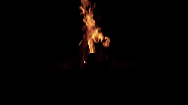 Upward tilting wide angle slow motion shot of logs burning vividly against a dark/black background while camping.