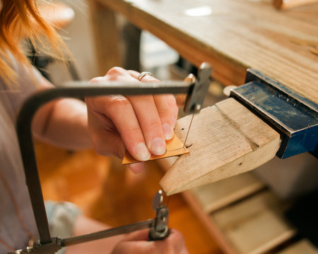 A young woman uses a saw to make a new piece of jewelry
