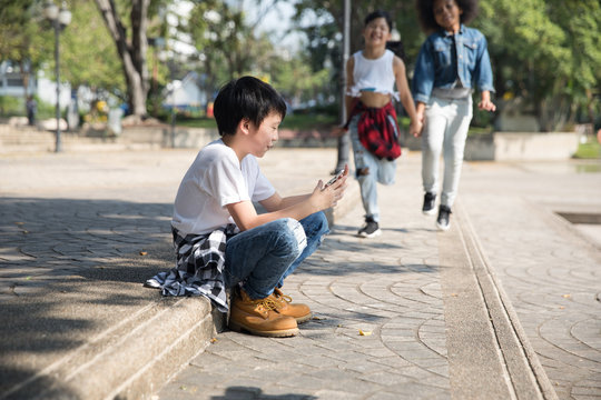 Cute boy on his phone, while two of his friends are approaching