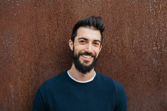 Handsome Smiling Man With Beard In Blue Pullover Over Rusty Background.