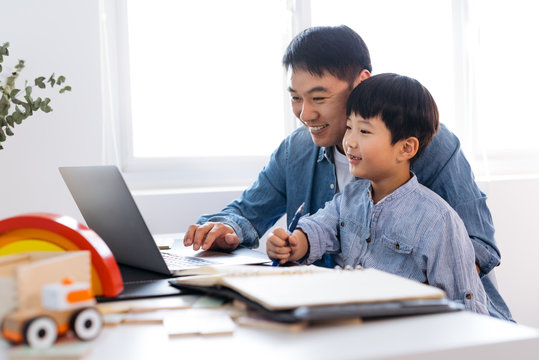 Boy sitting on father's lap behind desk in home office