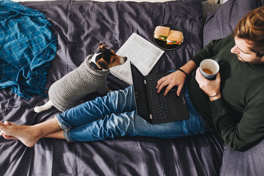 A Man Sitting on KIng-Size Bed and Using Laptop