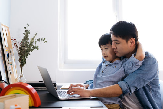 Boy sitting on father's lap behind desk in home office