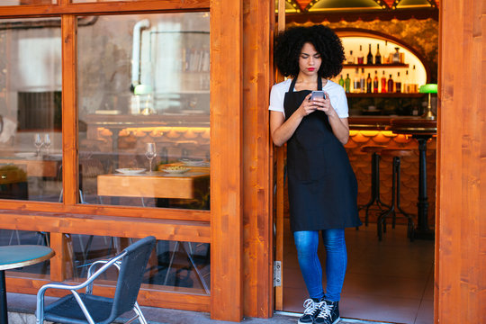 Waitress using her phone in front of a restaurant.