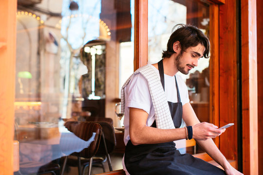 Waiter taking a break using his phone in front of a restaurant.