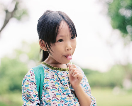 Asian little girl enjoying a lollipop in the park.shot by 120 films