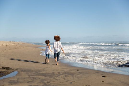 Curly haired mother and daughter running on a beach