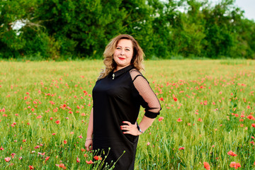 Plus sized woman in a black dress on a field of green wheat and wild poppies. Overweight fat woman.