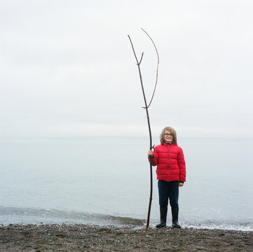Boy holds a rather long stick on a gravel beach on Bainbridge Island