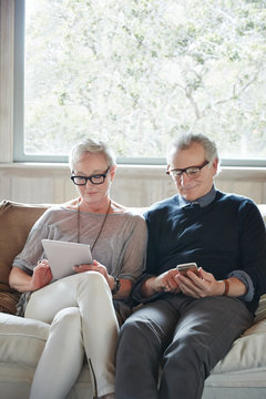 Mature couple with grey hair looking at digital tablet and phone at home