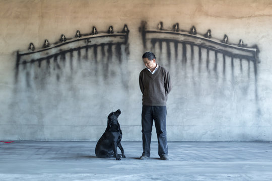 A man and dog in front of a wall with a gate painting on it
