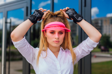 Portrait of an emotional girl in a pink cap visor and protective gloves for rollerblades and...