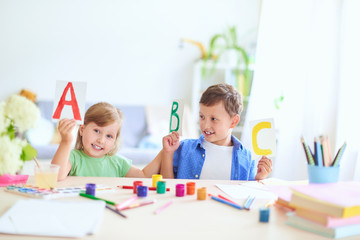 a little girl and a boy learn at home. happy kids at the table with school supplies smiling funny and learning the alphabet in a playful way.