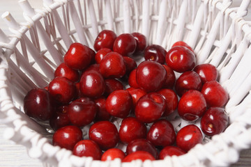 Red sweet cherries in a white basket on a white wooden table