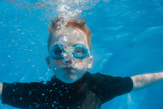 A young boy in a wetsuit blows air bubbles underwater