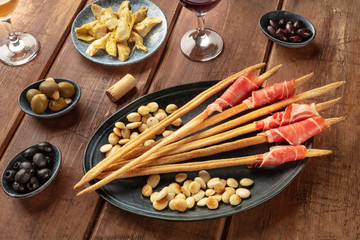 Italian antipasti. Grissini breadsticks with prosciutto di parma and roasted almonds, with olives and artichokes, with wine glasses