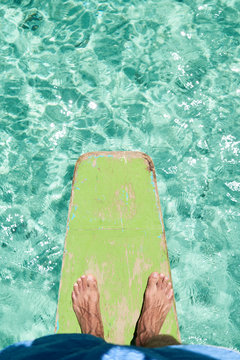 Overhead feet in prow with turquoise water on tropical beach.