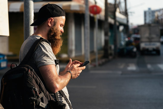 Portrait of hipster backpacker walking in the street. He is using mobile. Trip concept.