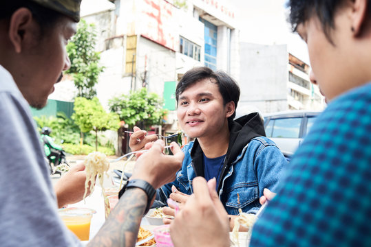 Asian friends eating street food outside.