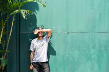Young man covering face with forearm outside.