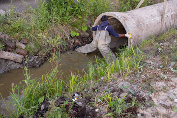Workers laid pipes in the drainage ditch. Red crane boom against the blue sky. Car manipulator...