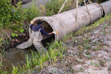 Workers laid pipes in the drainage ditch. Red crane boom against the blue sky. Car manipulator...