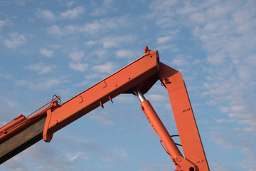 Red crane boom against the blue sky. Car manipulator unloads the pipe. Construction works. Summer. Sunny day.