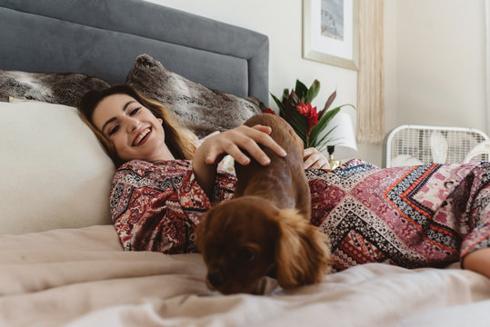 A woman in her twenties laying in bed with her dog