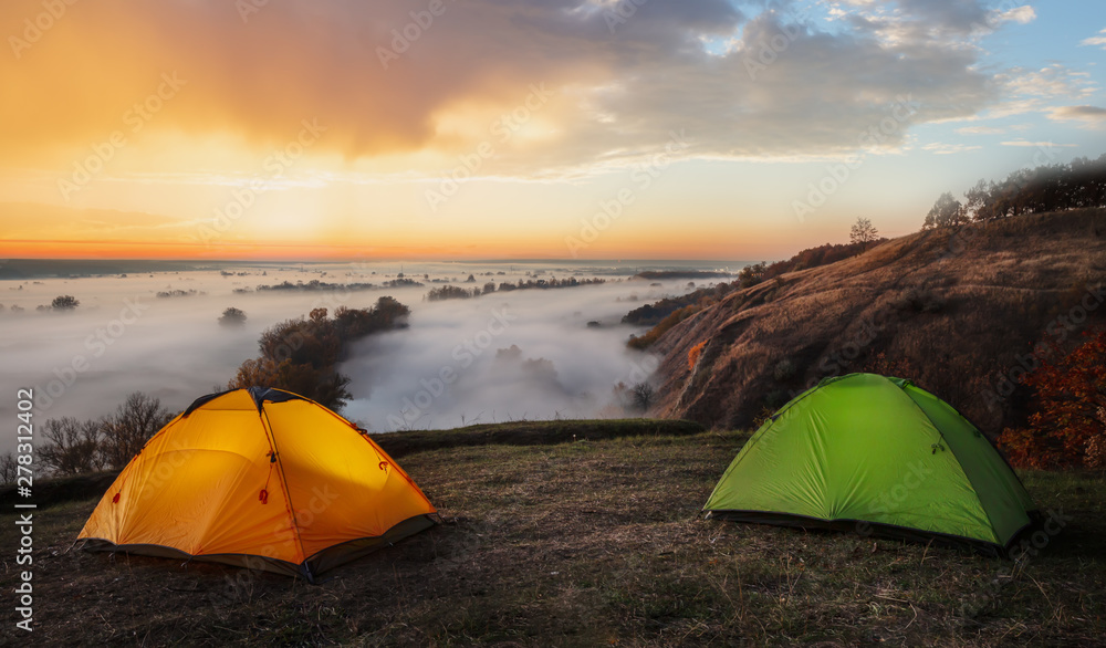 Wall mural orange and green tents over river sheltered by mist