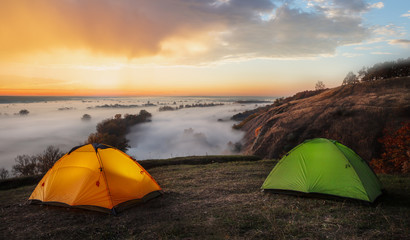 Orange and green tents over river sheltered by mist