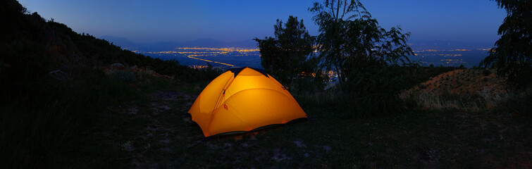 Orange illuminated inside tent on hill above city lights at night
