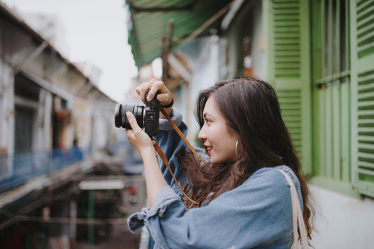 Young asian woman standing on balcony, taking photo of the old vintage house.