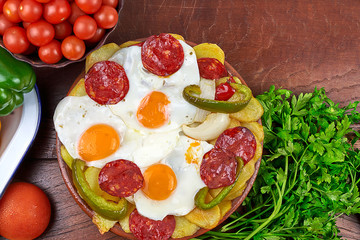 Fried eggs with chorizo accompanied by fried potatoes, onion and green pepper. A tomato salad with basil and some radishes. On the table, parsley, cherry tomatoes, purple onion and garlic.
