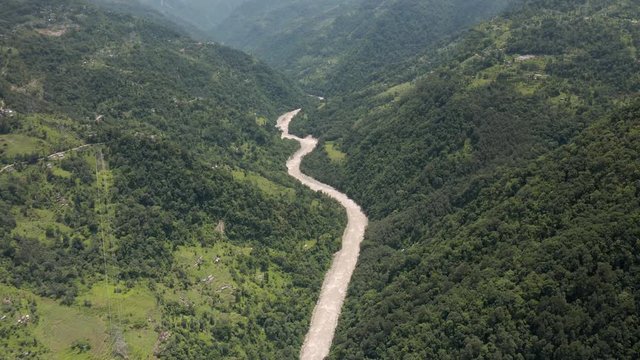 Aerial, tilt down, drone shot, above the Tista river, in a valley between mountains and Indian forest, on a sunny day, in Sikkim, India