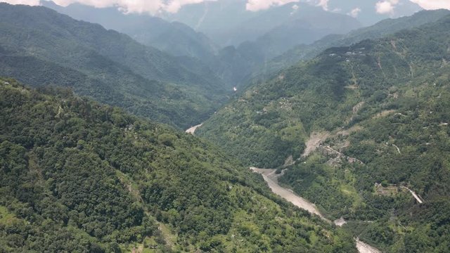 Aerial, tilt down, drone shot, above a valley between Himalayan mountains,overlooking the Tista river and green, Indian forest, on a partly sunny day, in Sikkim, India